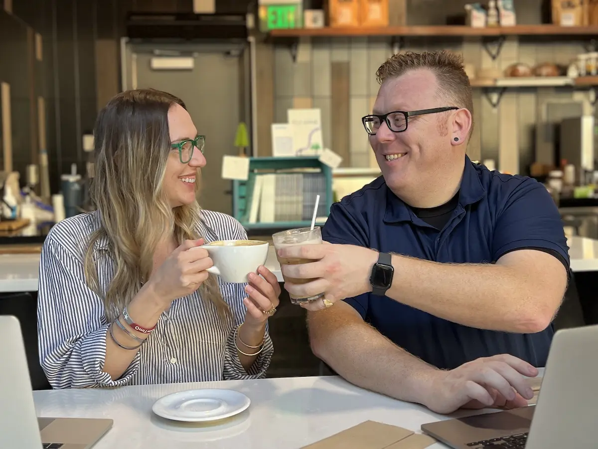PSI Seminars Podcast hosts Mackenzie and Tim smiling and toasting coffee drinks while working together at a café