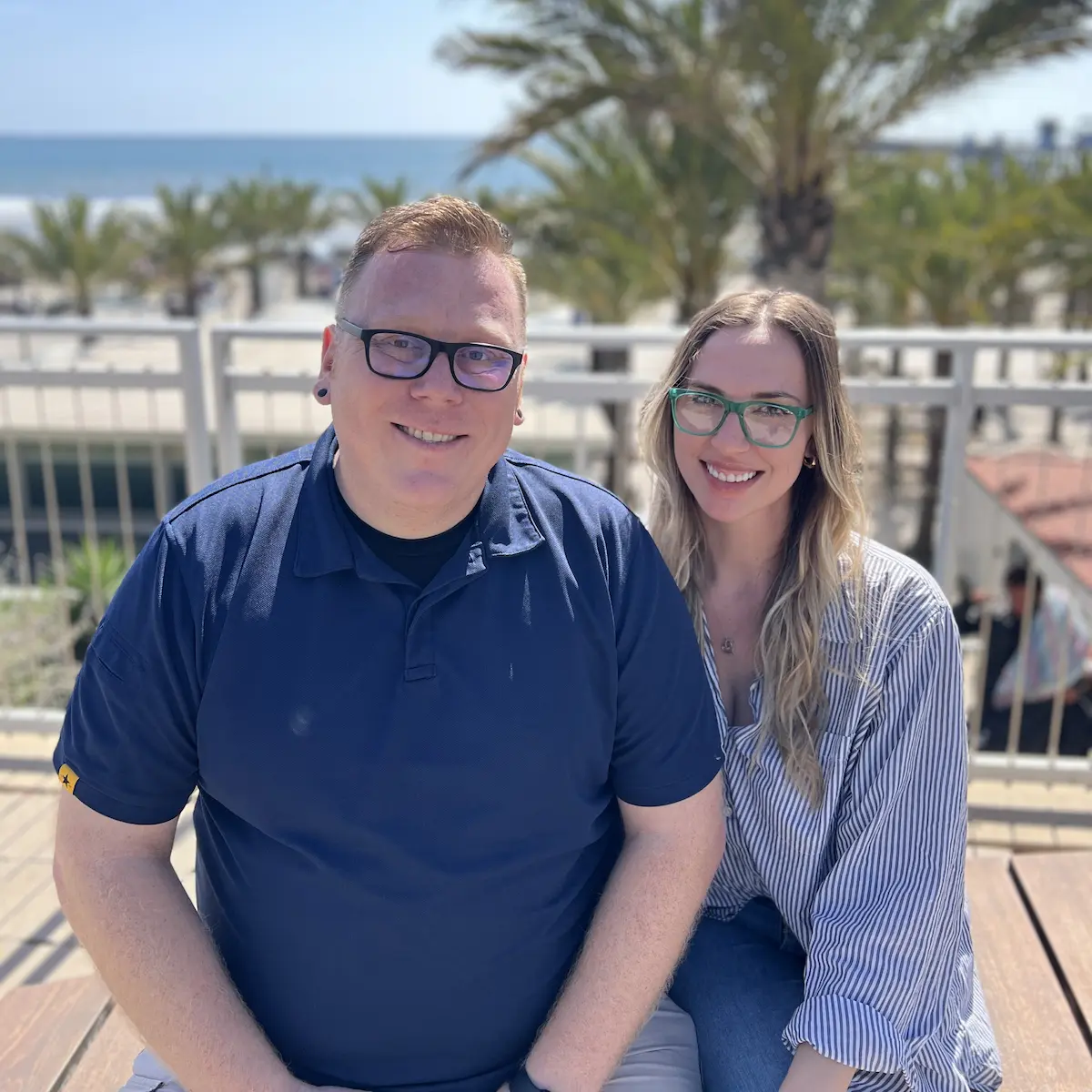 PSI Seminars Podcast hosts Tim and Mackenzie smiling outdoors near a beach with palm trees in the background